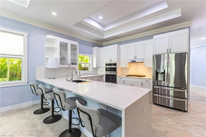 Kitchen featuring backsplash, a breakfast bar area, glass insert cabinets, appliances with stainless steel finishes, and a peninsula