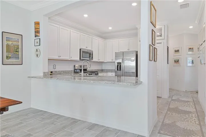 Kitchen with ornamental molding, light stone countertops, stainless steel appliances, white cabinetry, and recessed lighting