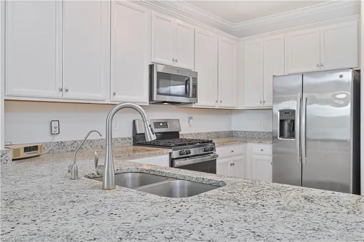 Kitchen with appliances with stainless steel finishes, light stone countertops, white cabinetry, and ornamental molding