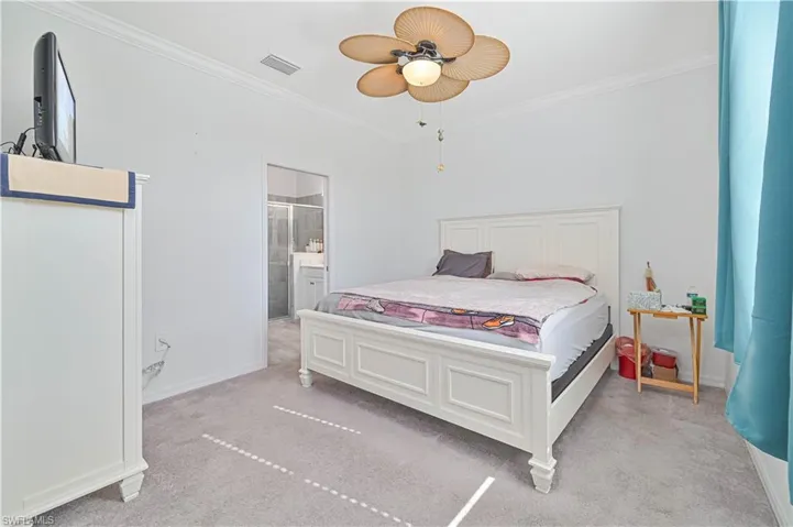 Bedroom with light colored carpet, ornamental molding, a ceiling fan, and connected bathroom