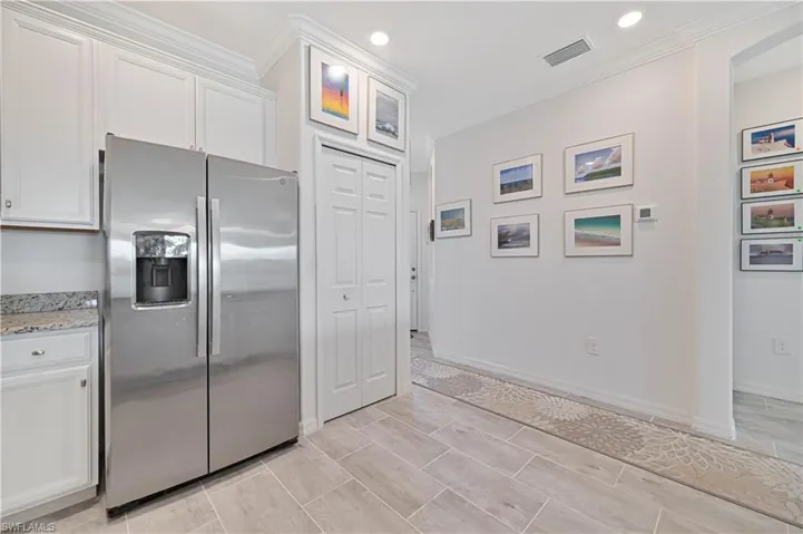 Kitchen with stainless steel fridge with ice dispenser, white cabinets, crown molding, light stone counters, and recessed lighting