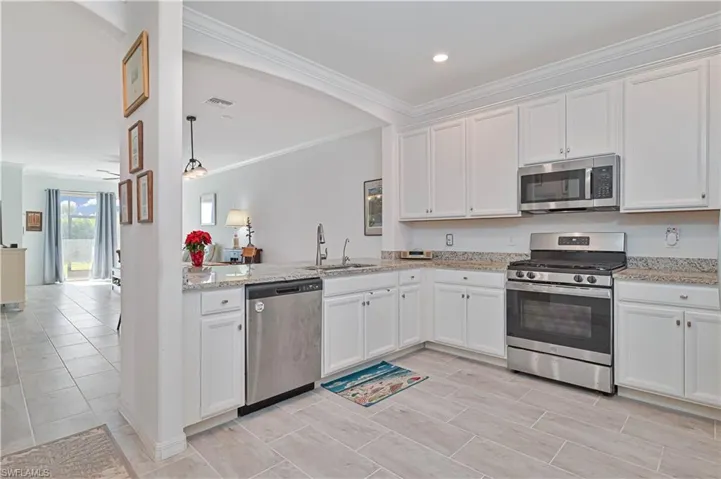 Kitchen featuring stainless steel appliances, white cabinets, ornamental molding, light stone countertops, and decorative light fixtures