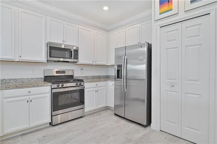 Kitchen featuring appliances with stainless steel finishes, white cabinets, light stone countertops, recessed lighting, and crown molding