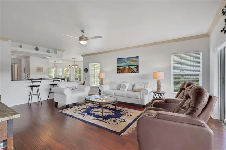 Living area with ceiling fan, dark wood finished floors, and ornamental molding
