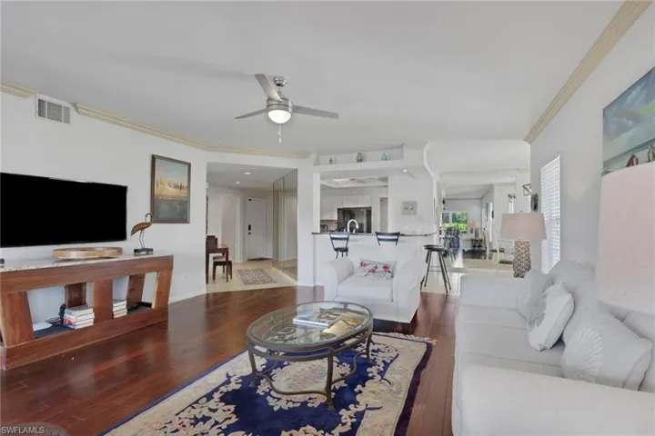 Living room with ceiling fan, dark wood-style flooring, and crown molding