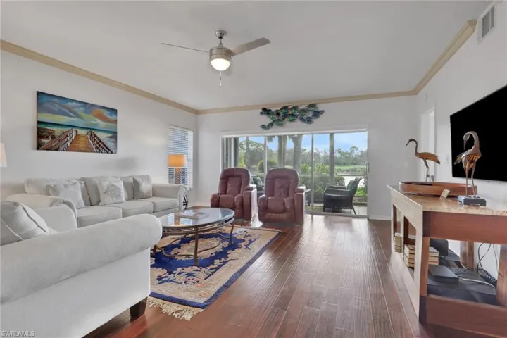 Living area featuring dark wood-style flooring, ornamental molding, and ceiling fan