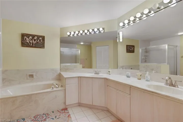 Full bath with double vanity, a garden tub, light tile patterned floors, and a shower stall