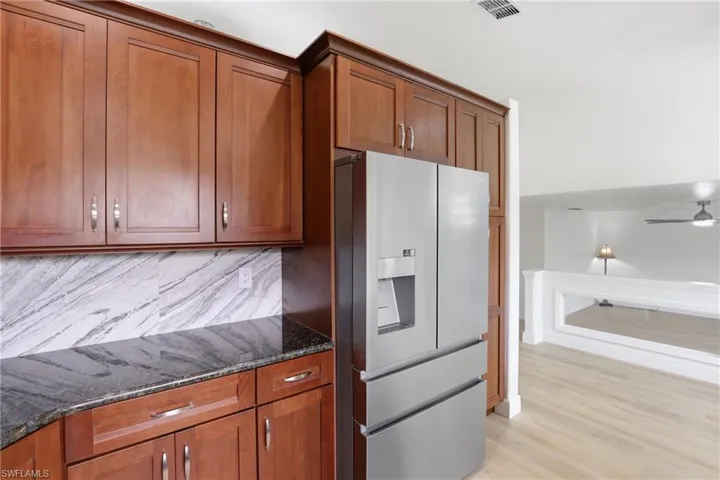 Kitchen with refrigerator with ice dispenser, dark stone counters, backsplash, wood finish cabinetry, and light wood finished floors