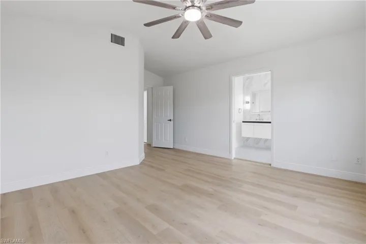 Unfurnished bedroom with a ceiling fan, light wood finished floors, lofted ceiling, and ensuite bathroom