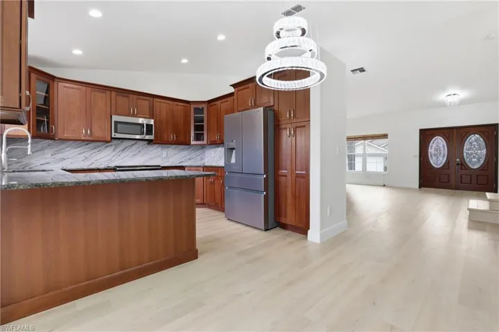 Kitchen with glass fronted cabinets, vaulted ceiling, dark stone countertops, stainless steel appliances, and backsplash