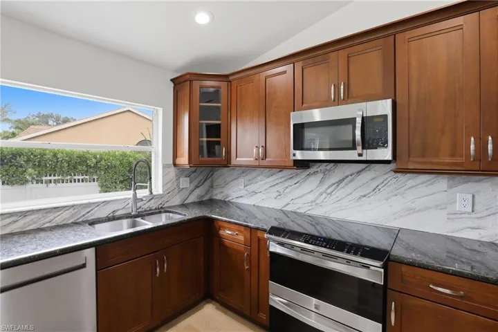 Kitchen with stainless steel appliances, dark stone counters, glass insert cabinets, vaulted ceiling, and backsplash