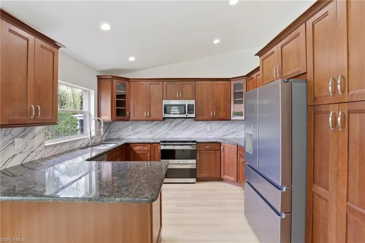 Kitchen featuring wood finish cabinetry, dark stone counters, glass insert cabinets, lofted ceiling, and recessed lighting