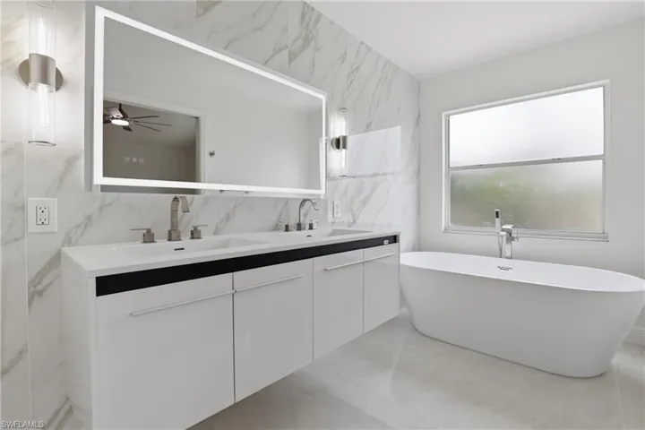 Bathroom featuring double vanity, a ceiling fan, a freestanding tub, and tile walls