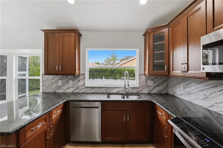 Kitchen with dark stone countertops, a peninsula, stainless steel appliances, glass insert cabinets, and decorative backsplash
