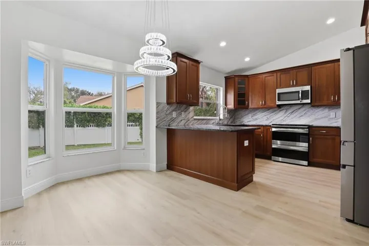 Kitchen featuring dark stone countertops, glass insert cabinets, a peninsula, stainless steel appliances, and vaulted ceiling