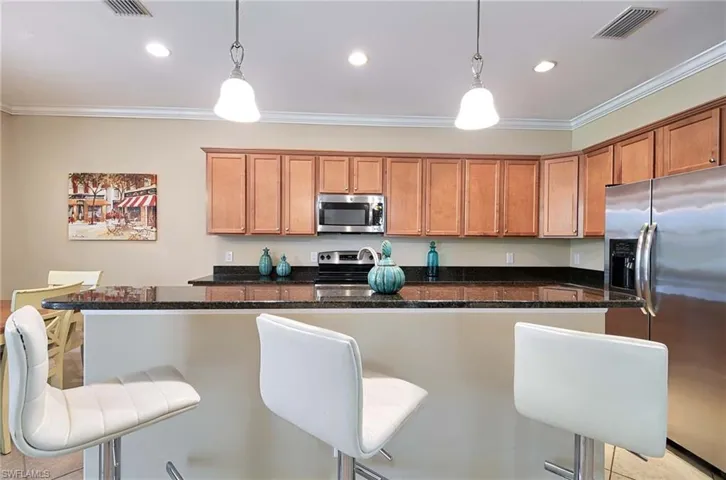 Kitchen with appliances with stainless steel finishes, brown cabinetry, ornamental molding, a breakfast bar area, and pendant lighting
