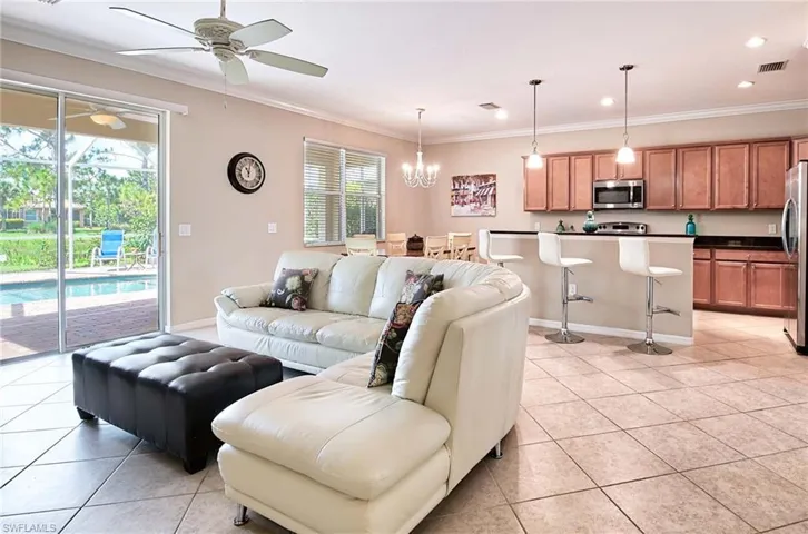 Living room with a ceiling fan, crown molding, light tile patterned flooring, baseboards, and a chandelier