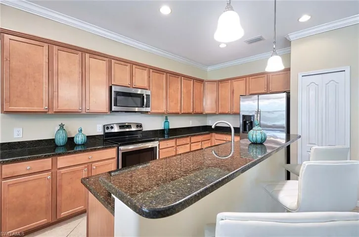 Kitchen with appliances with stainless steel finishes, a breakfast bar area, decorative light fixtures, ornamental molding, and dark stone counters