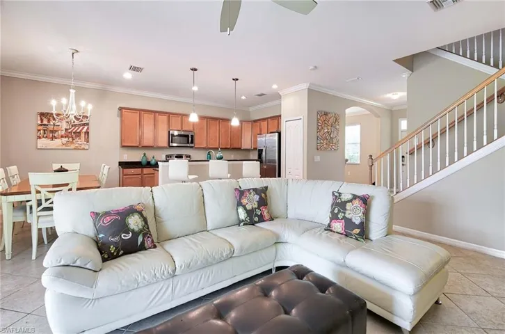 Living room featuring a chandelier, light tile patterned flooring, arched walkways, ceiling fan, and stairs