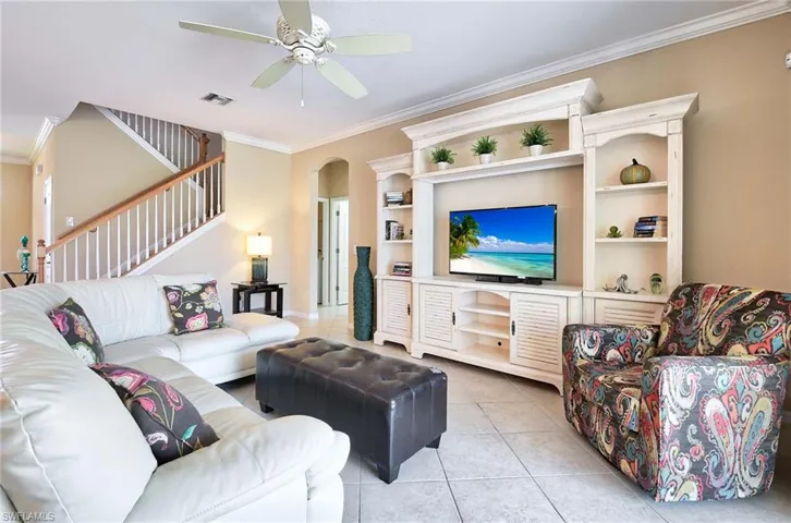 Living area featuring crown molding, light tile patterned flooring, a ceiling fan, arched walkways, and stairs