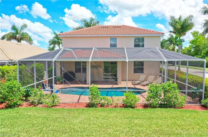 Back of property with stucco siding, a lanai, a tiled roof, an outdoor pool, and a lawn