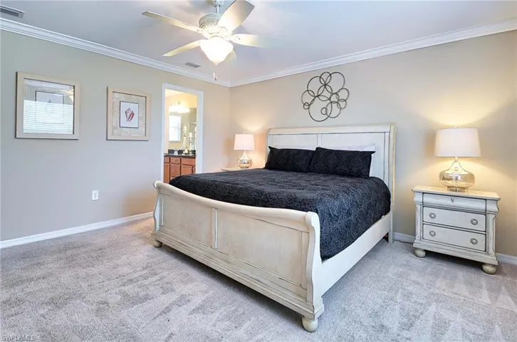 Bedroom featuring carpet floors, crown molding, baseboards, ceiling fan, and ensuite bath