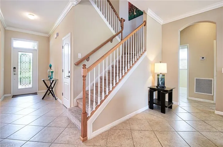 Tiled entrance foyer featuring arched walkways, ornamental molding, baseboards, and stairs