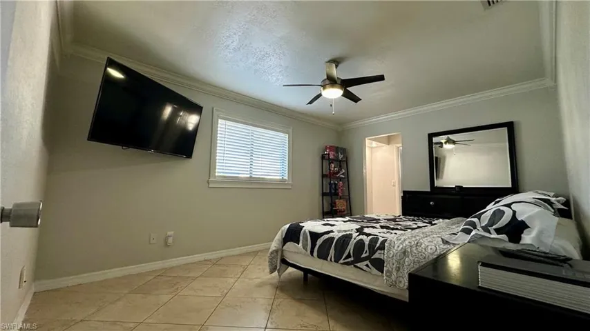 Tiled bedroom featuring ceiling fan and ornamental molding