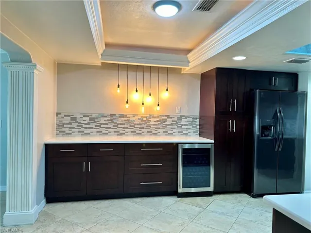 Kitchen with refrigerator with ice dispenser, wine cooler, dark brown cabinets, and decorative backsplash