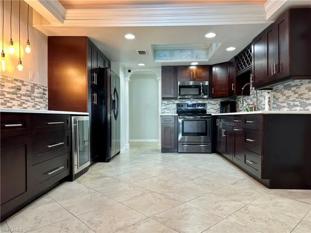 Kitchen featuring tasteful backsplash, beverage cooler, stainless steel appliances, dark brown cabinetry, and ornamental molding