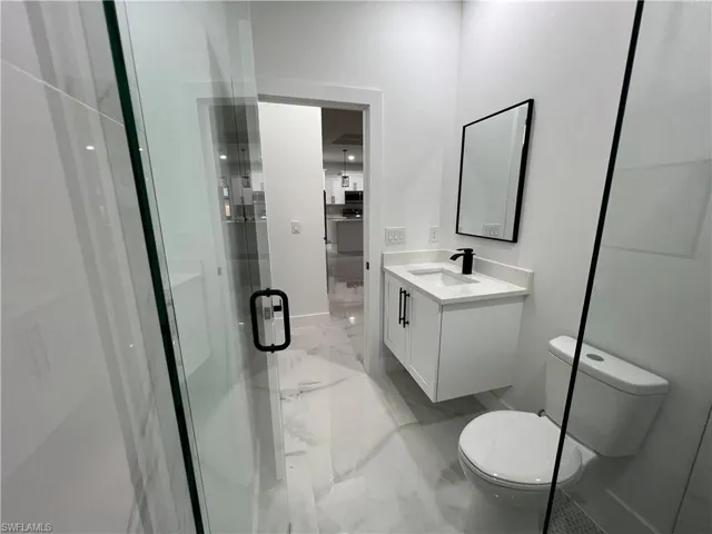 Bathroom with oversized vanity, toilet, tile floors, and a shower with door