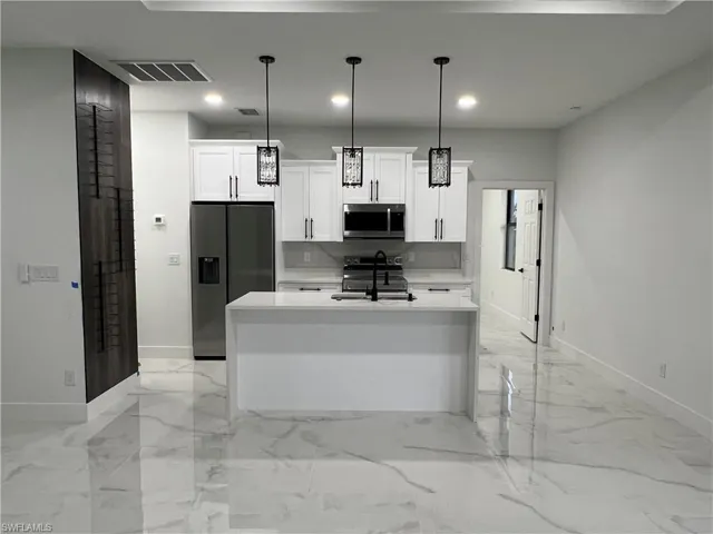 Kitchen featuring light tile flooring, hanging light fixtures, white cabinets, a kitchen island with sink, and appliances with stainless steel finishes