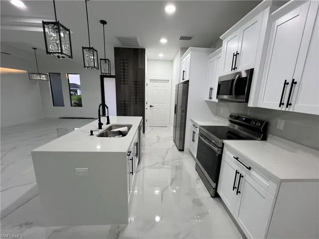 Kitchen with stainless steel appliances, an island with sink, white cabinets, decorative light fixtures, and sink