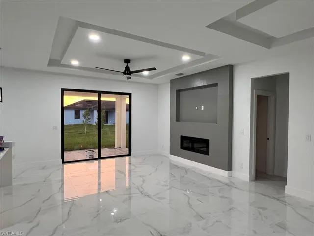 Unfurnished living room with ceiling fan, a tray ceiling, and light tile floors