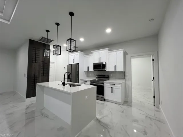 Kitchen featuring a center island with sink, pendant lighting, light tile floors, white cabinets, and appliances with stainless steel finishes