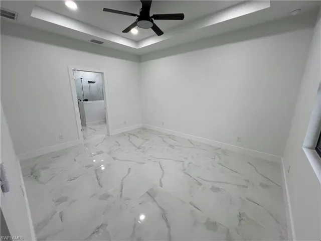 Unfurnished room featuring a tray ceiling, ceiling fan, and light tile floors