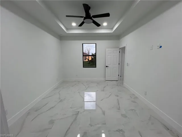 Empty room featuring a raised ceiling, ceiling fan, and light tile floors
