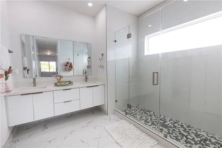 Bathroom with a shower stall, double vanity, marble finish floors, and recessed lighting