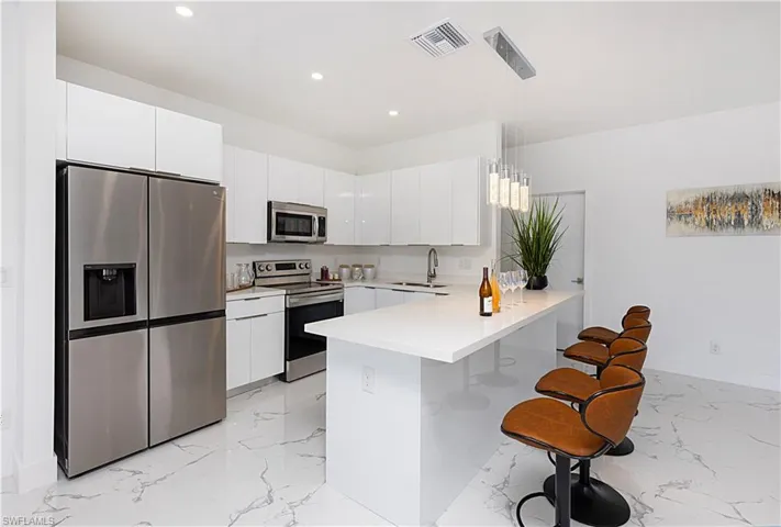 Kitchen with stainless steel appliances, a peninsula, light marble finish flooring, recessed lighting, and a breakfast bar area