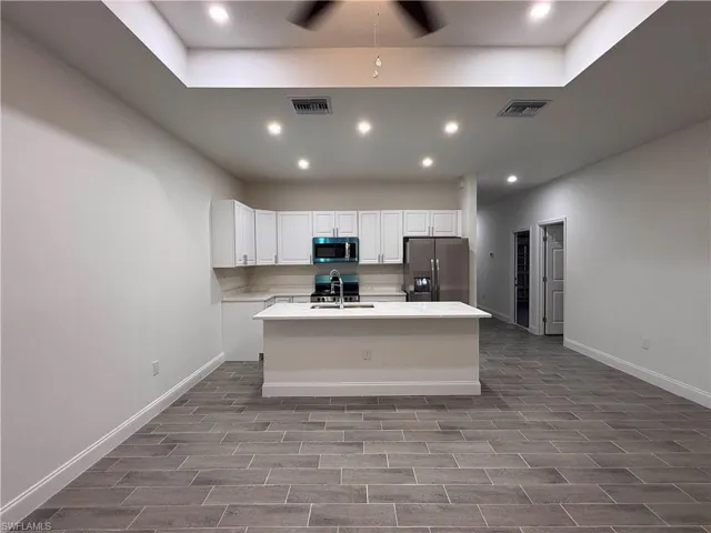 Kitchen with stainless steel appliances, a center island with sink, white cabinetry, recessed lighting, and wood finish floors