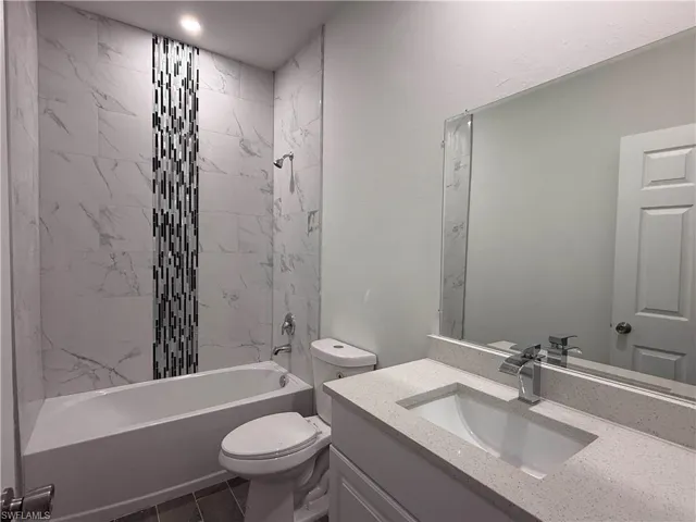 Full bath featuring vanity, washtub / shower combination, and dark tile patterned flooring