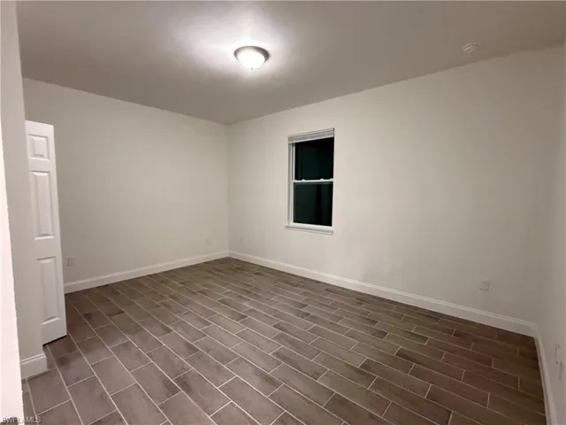 Empty room with baseboards and dark wood-type flooring