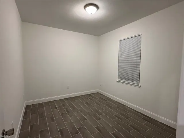 Unfurnished room featuring baseboards and dark wood-style floors