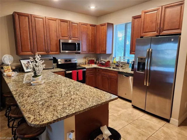 Kitchen with a breakfast bar, stainless steel appliances, kitchen peninsula, and light stone countertops