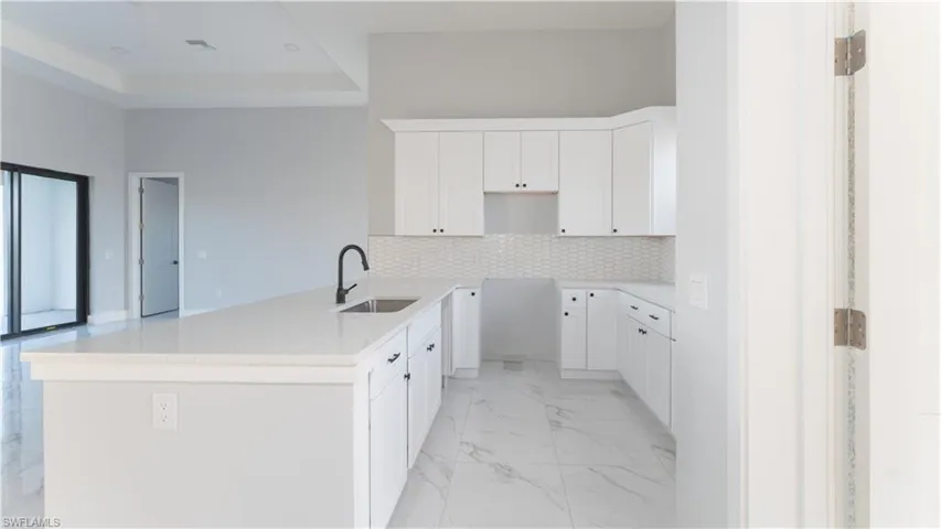 Kitchen with kitchen peninsula, decorative backsplash, white cabinetry, and sink