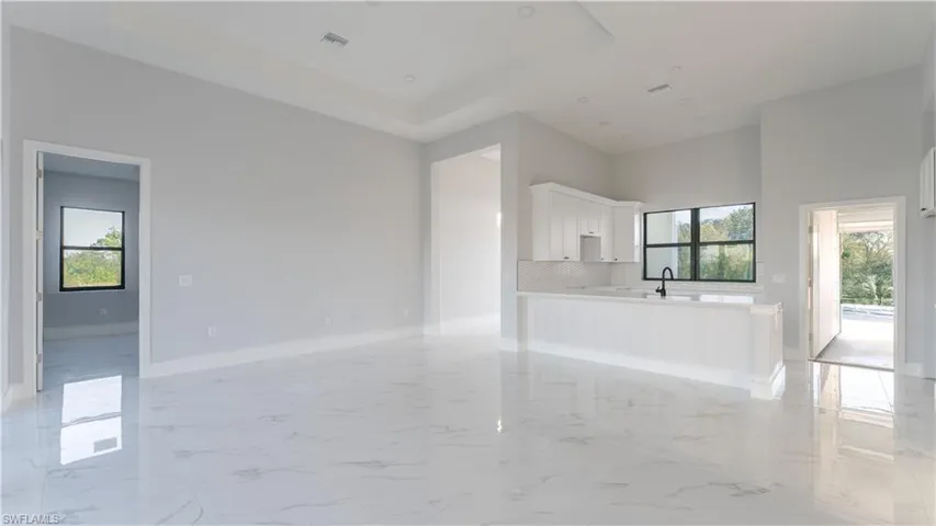 Unfurnished living room featuring a healthy amount of sunlight, a raised ceiling, sink, and a high ceiling