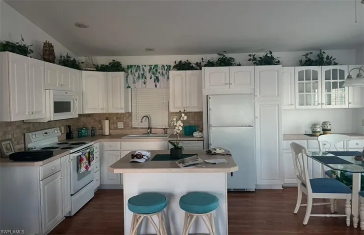 Kitchen with sink, white appliances, white cabinetry, a kitchen island, and dark hardwood / wood-style flooring
