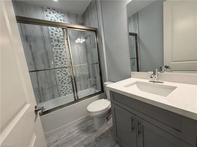 Full bathroom featuring enclosed tub / shower combo, vanity, and toilet