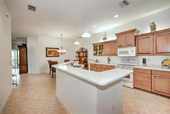 Kitchen with white appliances, light tile patterned floors, an inviting chandelier, a kitchen island with sink, and pendant lighting