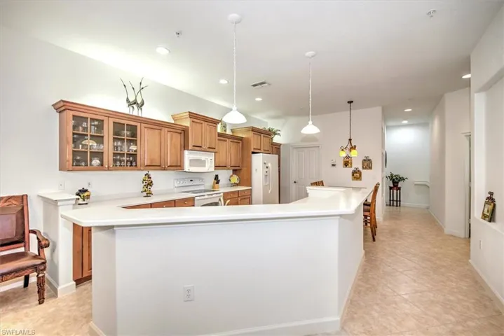 Kitchen featuring a breakfast bar area, white appliances, kitchen peninsula, hanging light fixtures, and light tile patterned floors